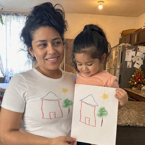 Mom in a white tee printed with a kid's house drawing, next to the paper original