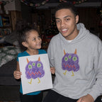 Big brother in a sport grey hoodie printed with a kid's monster drawing, next to the paper original